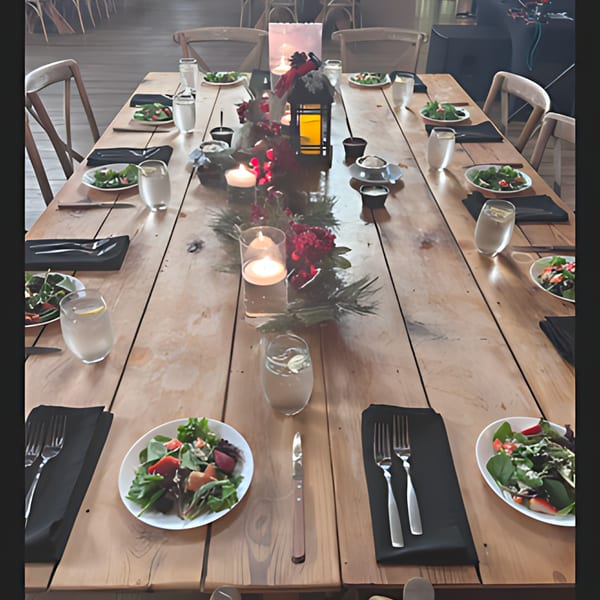 Long wooden table set for a Latin-American dinner with salads, candles, and festive red decor.