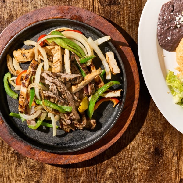 Sizzling D Restaurant Latin Cuisine fajitas with steak, chicken, onions, and peppers on a wooden table.