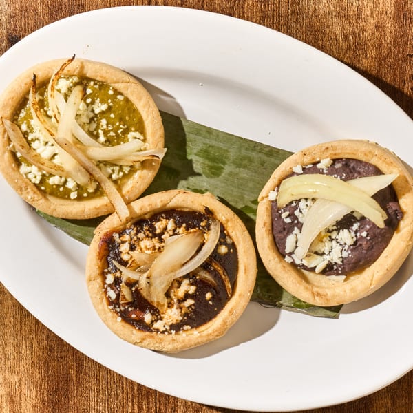 Three Latin American sopes with green salsa, mole, and black beans, topped with cheese and onions.