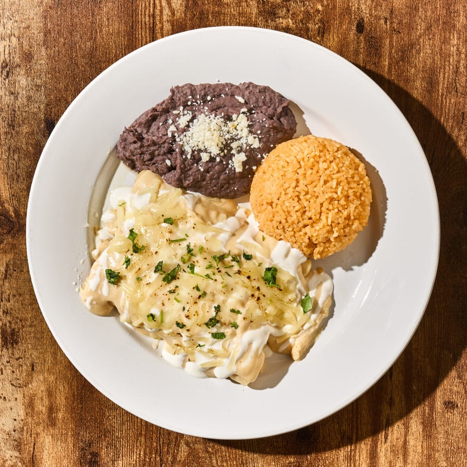 Latin-American dish with enchiladas, refried beans, and rice on a white plate.