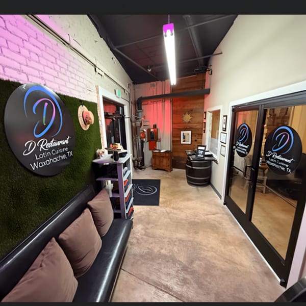 Interior view of D Restaurant's waiting area with a black couch, green wall, and entrance doors.