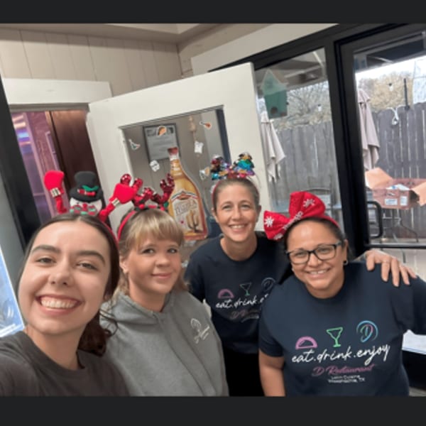 Four smiling D Restaurant staff members wearing festive headbands and branded t-shirts.