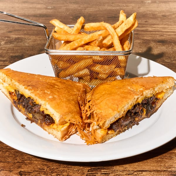 A Latin-American grilled cheese sandwich with dark meat and cheese, served with a side of fries.