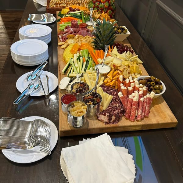 A large charcuterie board with meats, cheeses, fruits, vegetables, and dips, alongside stacks of plates and cutlery.