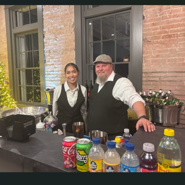Two D Restaurant Latin Cuisine bartenders smiling behind a bar with drinks and bottles.