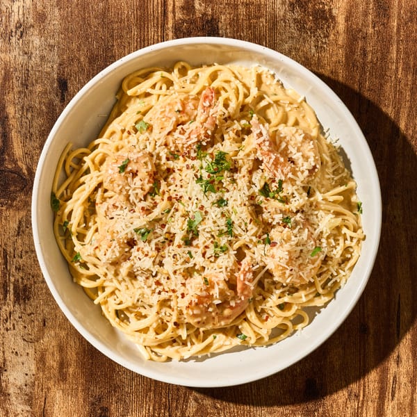 Creamy shrimp pasta with grated cheese, red pepper flakes, and parsley in a white bowl.