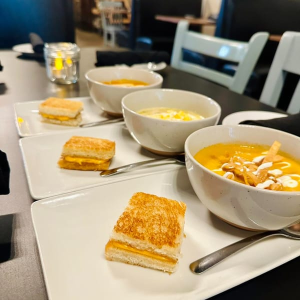 Three bowls of Latin-American soup with tortilla strips and three grilled cheese sandwiches on white plates.