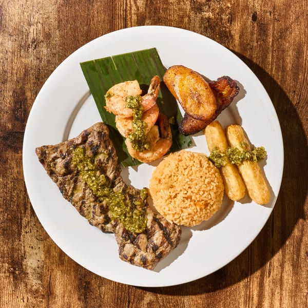 Latin-American dish with grilled steak, shrimp, rice, plantains, and yuca fries on a white plate.
